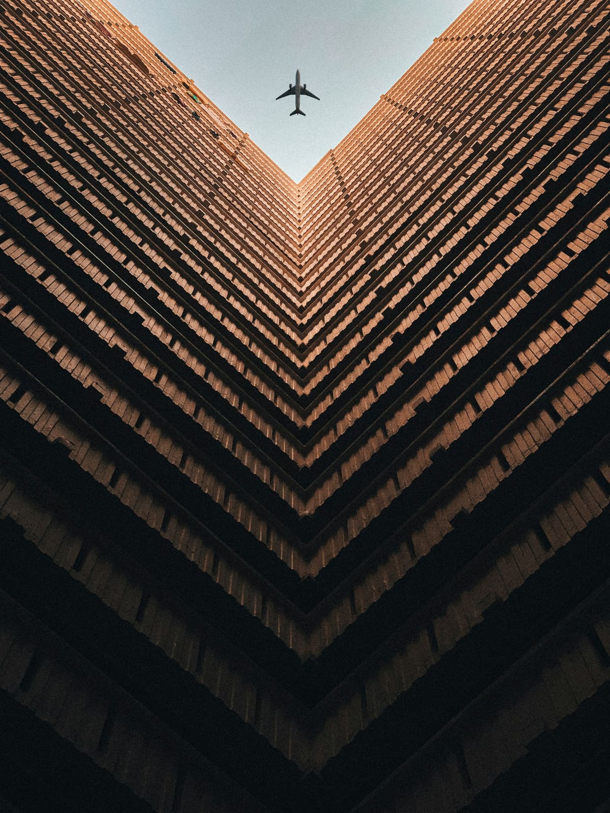 Looking up the corner of a tall brick building as an aircraft passes overhead